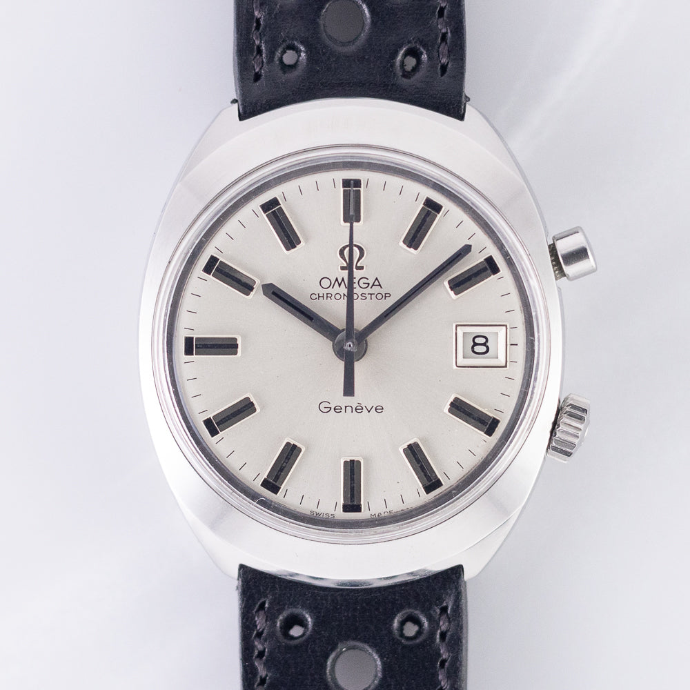 Japanese-market Chronostop Date: sunburst silver dial with wide polished applied bar markers filled in black, applied Omega logo, framed date at three, polished chronograph hand and no lume, in the polished-edge Genève case. The dealer notes the non-luminous dial with black print. · Photo: Time Anagram · © Time Anagram, used with permission · Source: https://timeanagram.com/products/31125